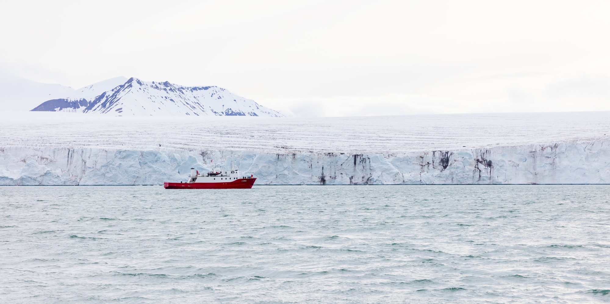 Expedition or tourist boat in front of the large and massive Borebreen glacier. Arctic environment in Oscar II Land at Spitsbergen, Svalbard.
